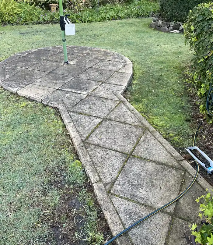 Grimy, moss-stained stone patio circle set in a lawn, before pressure washing