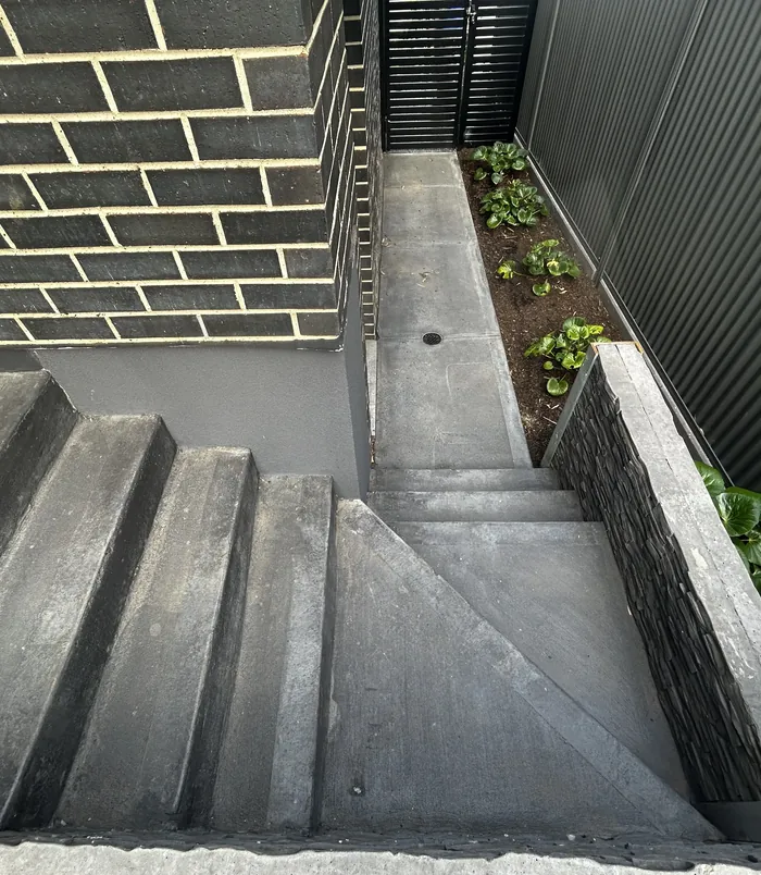 Stained concrete steps and side path between a dark brick wall and a fence, before resurfacing
