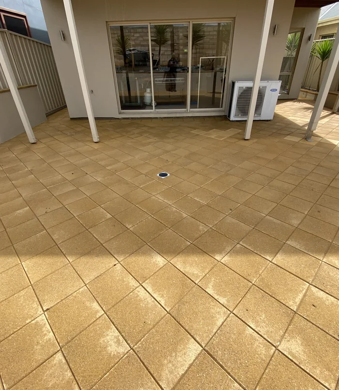 Clean, warm-toned pavers under a pergola beside sliding glass doors after pressure washing
