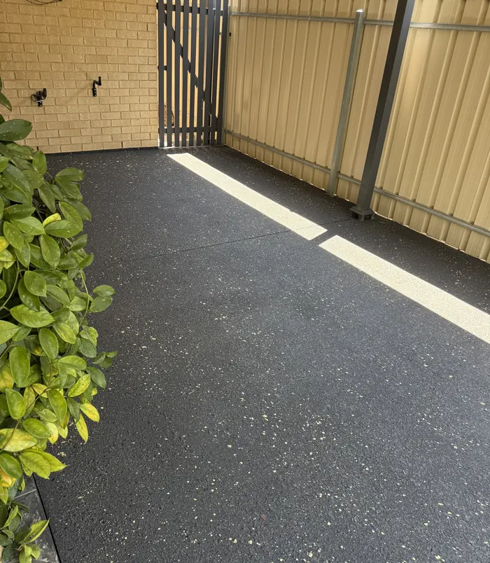 Dark speckled resurfaced concrete courtyard beside a gate, fence and plants