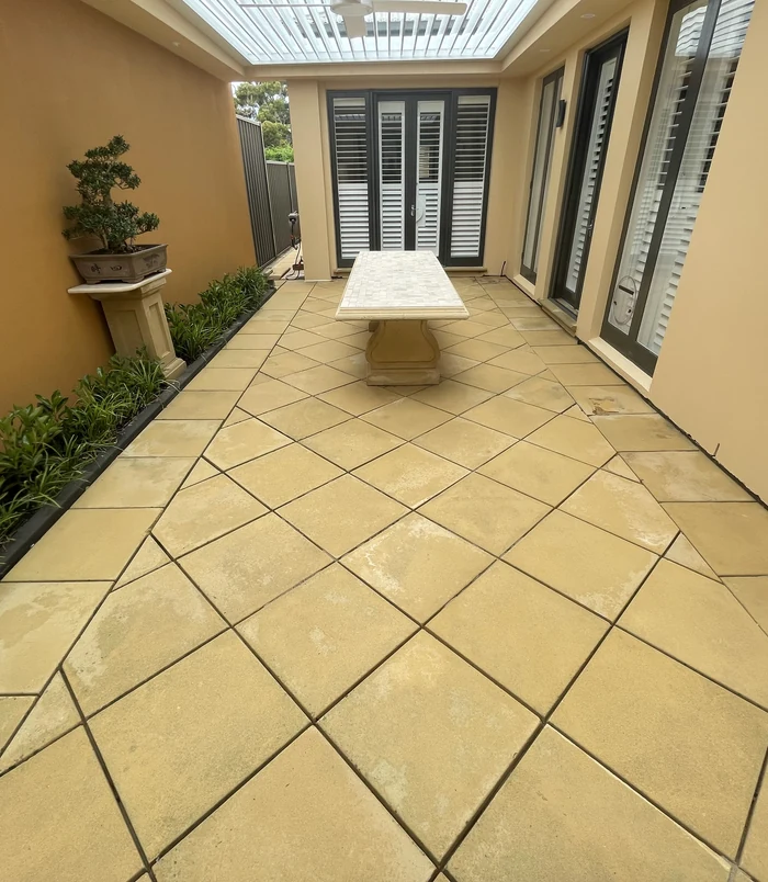 Clean, golden pavers in a covered courtyard with a stone table and shuttered doors after pressure washing
