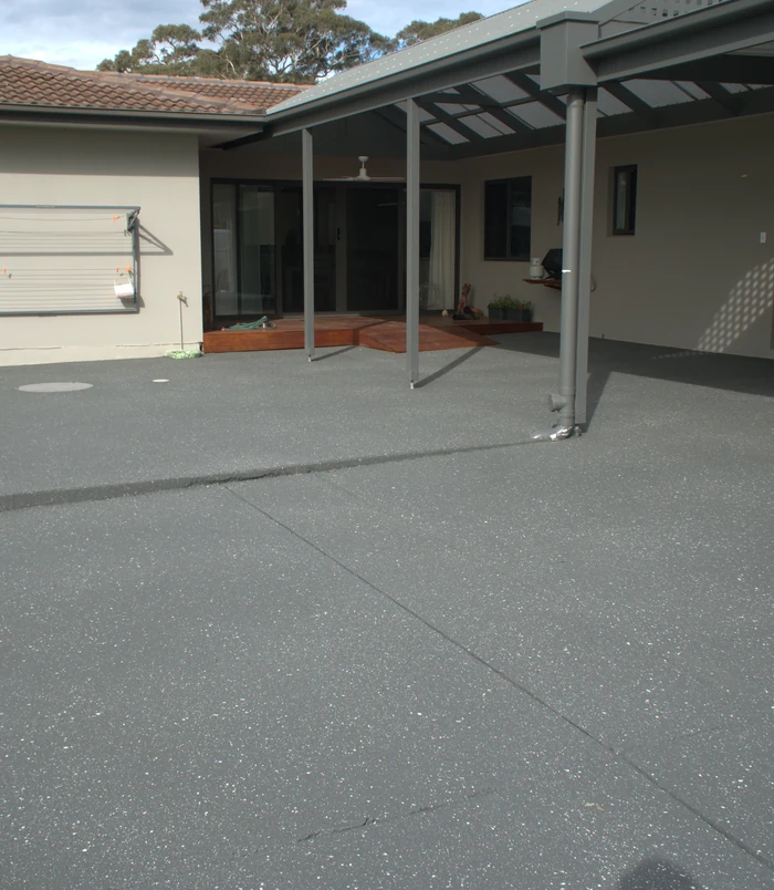 Smooth grey resurfaced concrete patio under a pergola beside a house