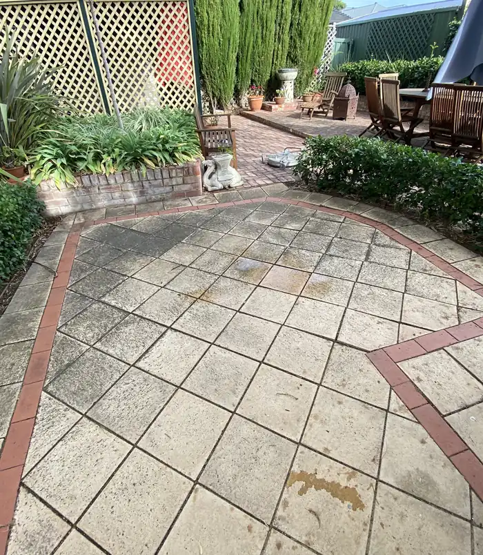 Dull, dirty patterned pavers with a red border in a garden courtyard, before pressure washing
