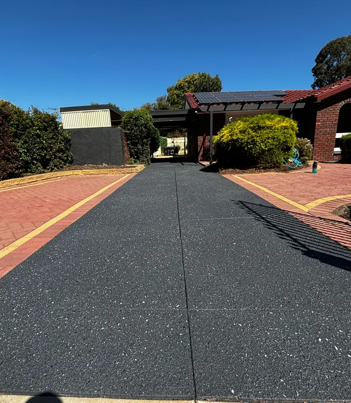 Dark resurfaced concrete driveway with red brick paving edges leading to a home