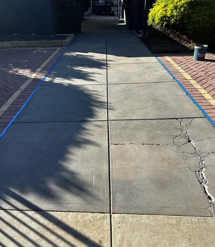 Pale, cracked concrete driveway with blue masking tape beside brick paving, before resurfacing