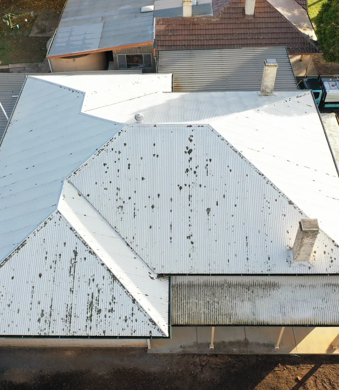 Light roof with dark spots of dirt and debris, viewed from above, before pressure washing