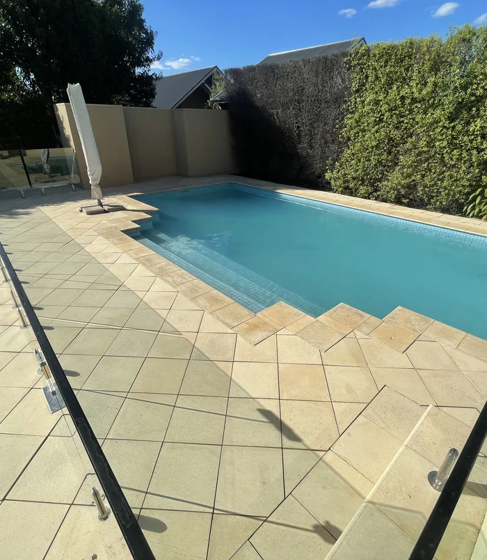 Clean, light-coloured pool surround and steps beside a swimming pool after pressure washing