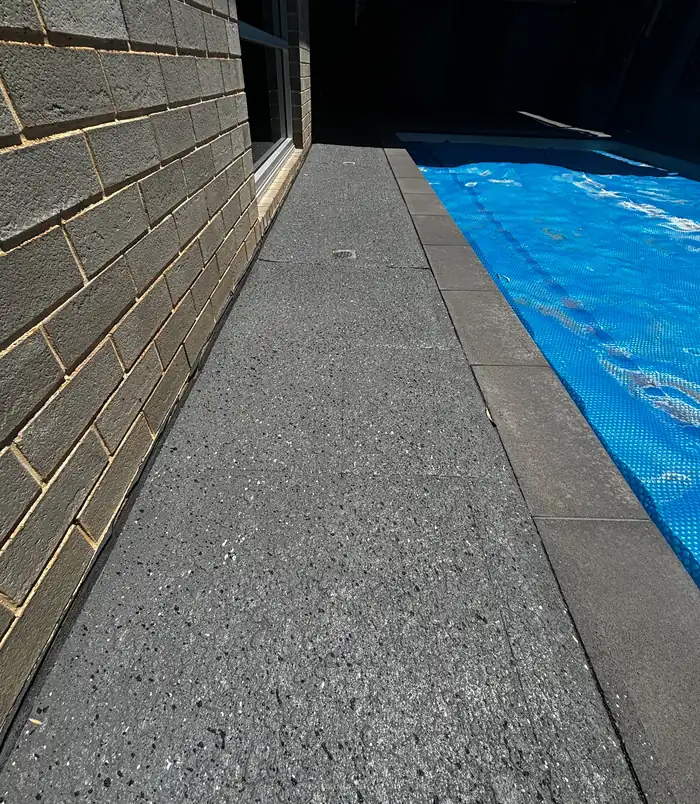 Speckled grey resurfaced concrete pool surround beside a brick wall and pool cover