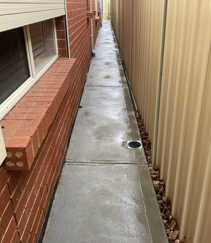 Clean concrete side path between a brick wall and a tan fence after pressure washing