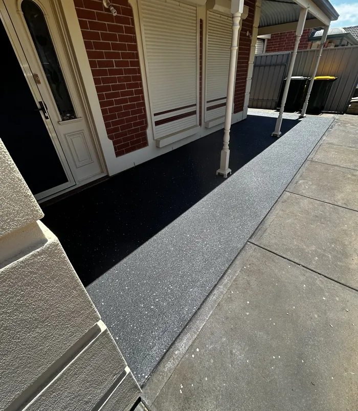 Dark resurfaced concrete veranda floor with a pale border beside a brick wall