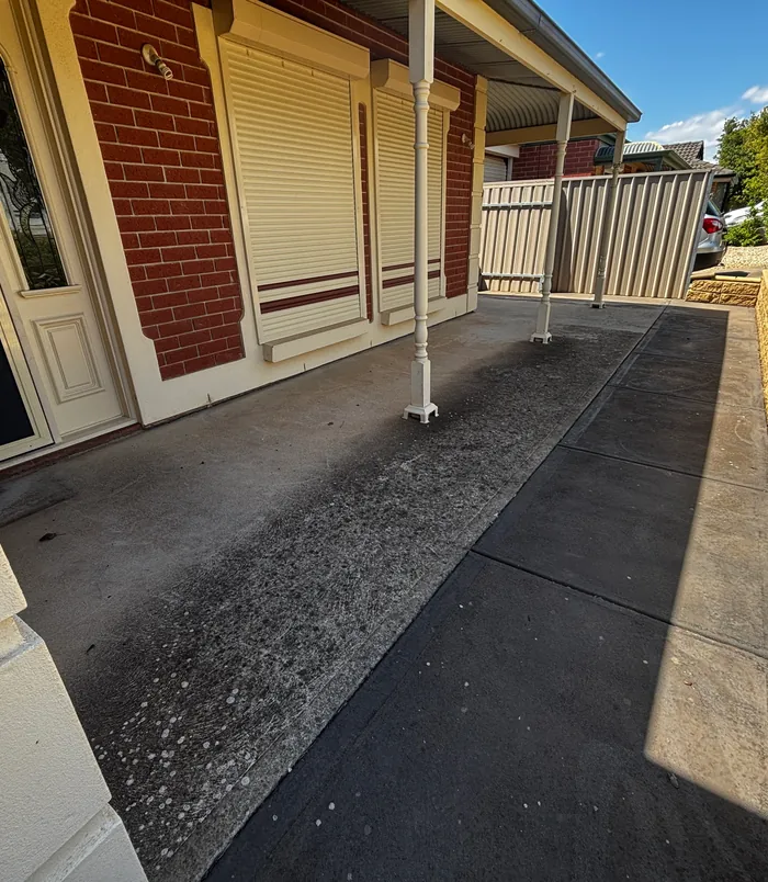 Worn, stained concrete veranda floor beside a brick wall with roller shutters, before resurfacing