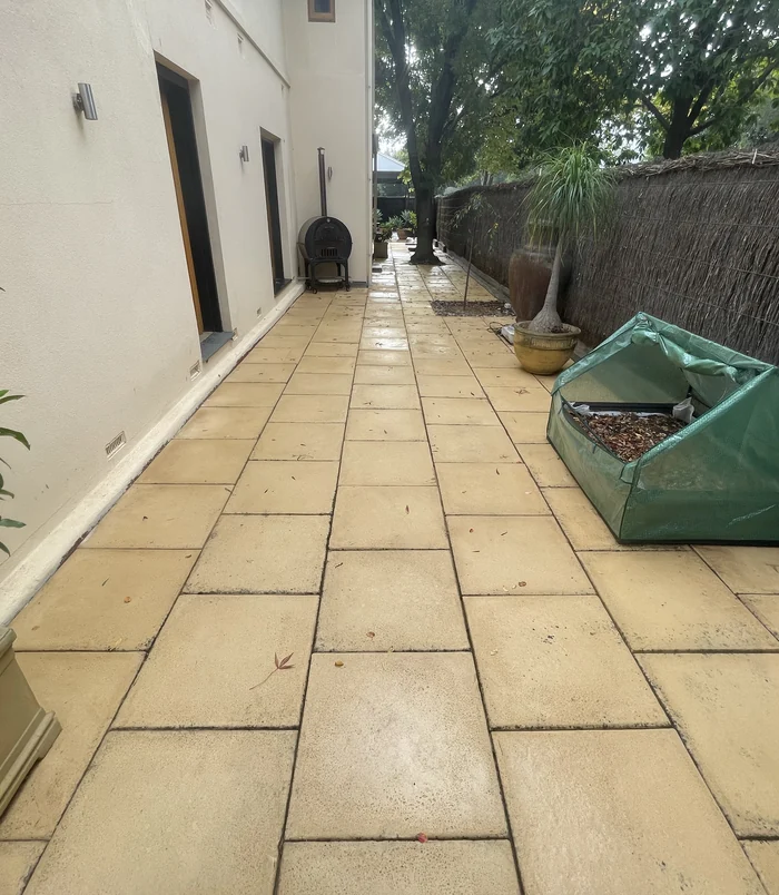 Clean, golden pavers in a side courtyard beside a rendered wall and garden bed after pressure washing