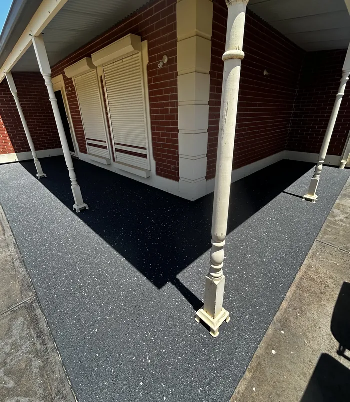Dark resurfaced concrete patio under a veranda beside a brick wall and roller shutters