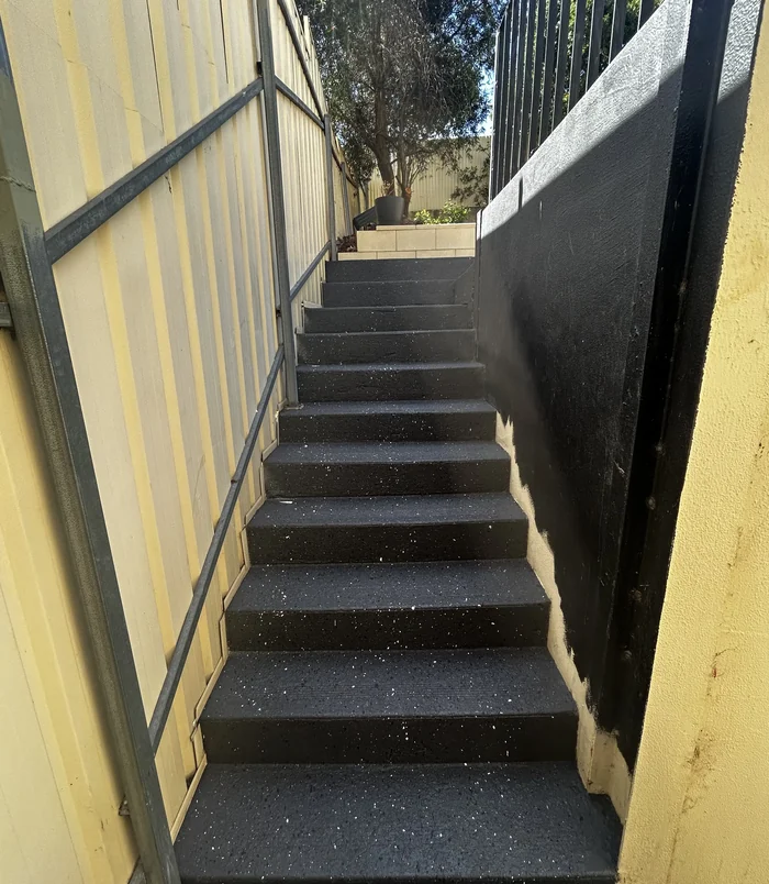 Dark grey resurfaced concrete steps between a fence and a wall