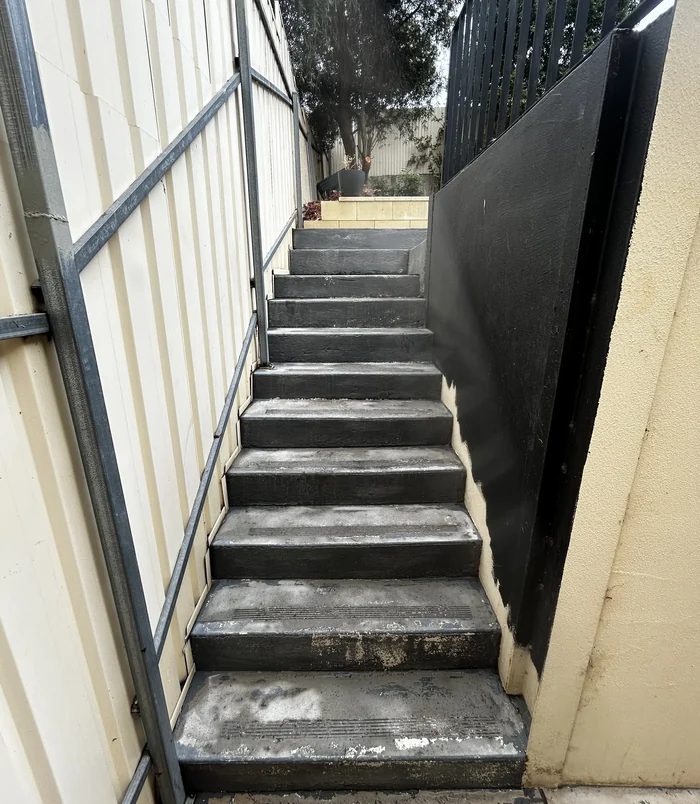 Pale concrete steps between a fence and a dark wall, before concrete resurfacing