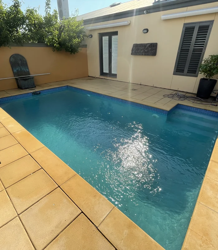 Clean, golden pavers around a small blue swimming pool in a courtyard after pressure washing