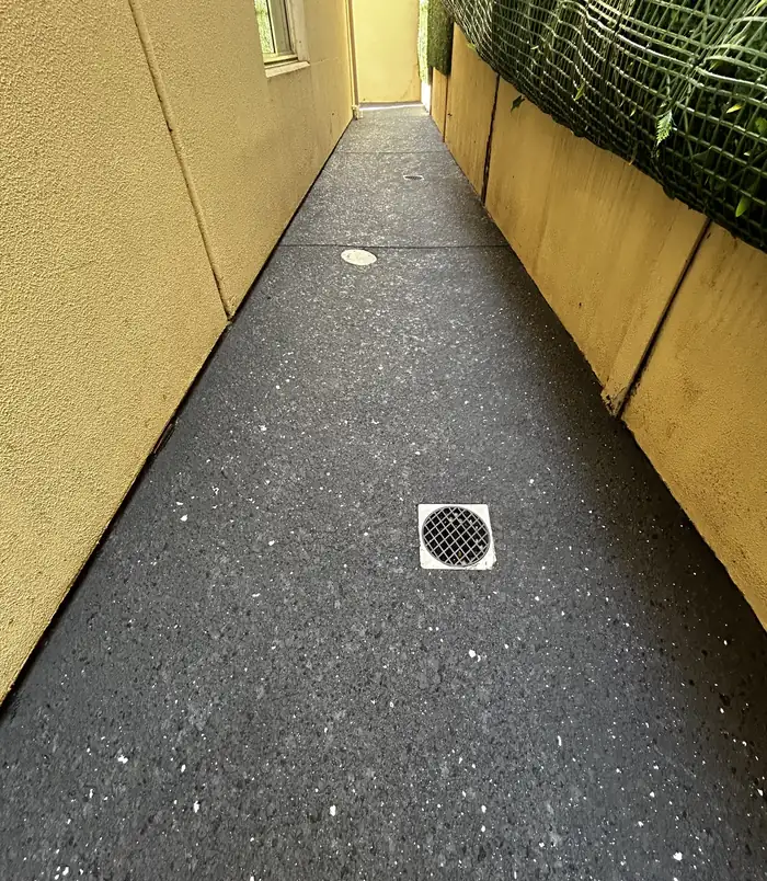 Dark speckled resurfaced concrete side path between two walls