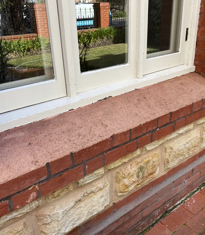 Clean red brick ledge beneath white-framed windows after pressure washing
