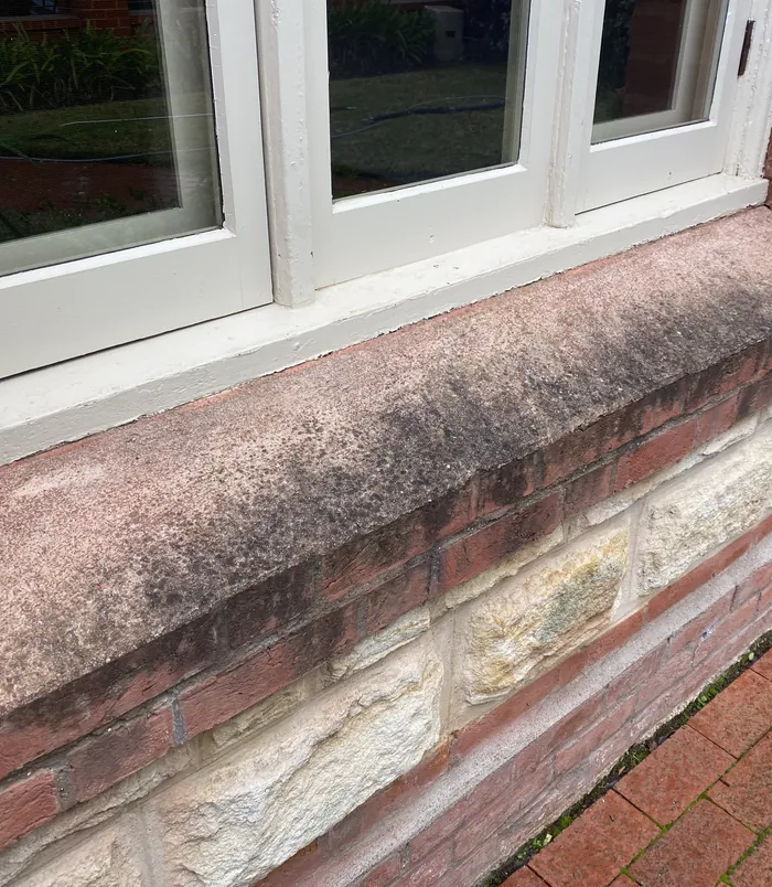 Dirty, faded window sill and brick ledge beneath white-framed windows, before pressure washing