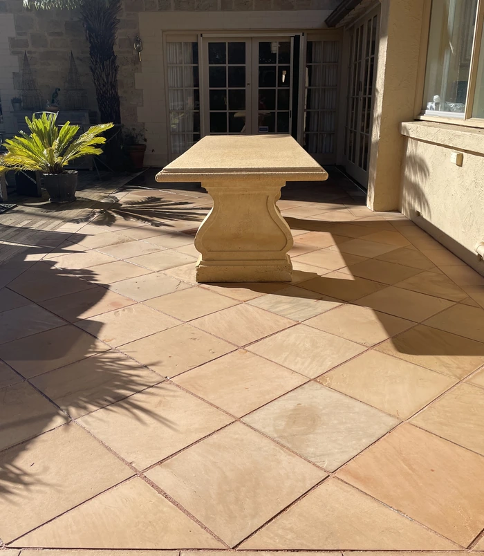 Clean terracotta pavers around a stone outdoor table beside French doors after pressure washing