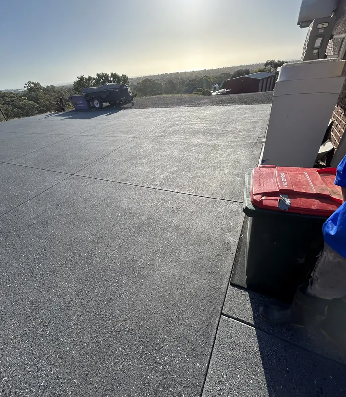 Dark grey resurfaced concrete driveway with wheelie bins beside a house