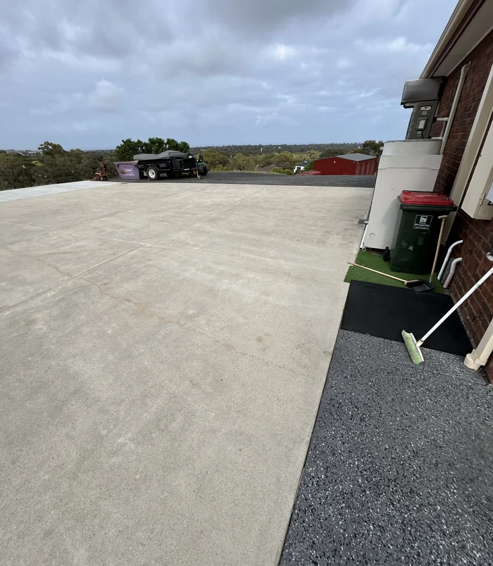 Pale, stained concrete driveway with wheelie bins beside a house, before concrete resurfacing