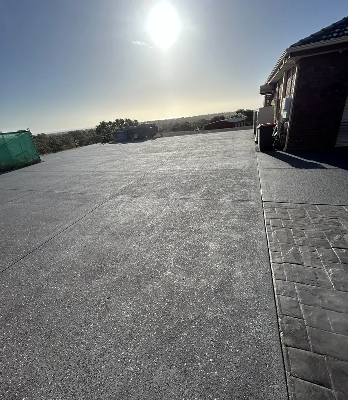 Large dark grey resurfaced concrete driveway area beside a brick house