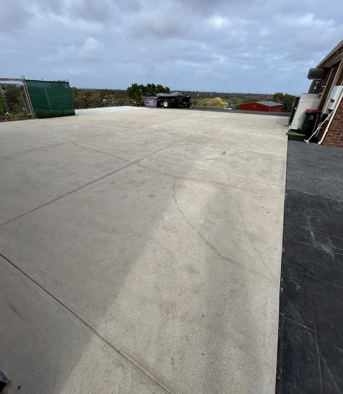 Large, pale concrete driveway area with bins beside a house, before concrete resurfacing