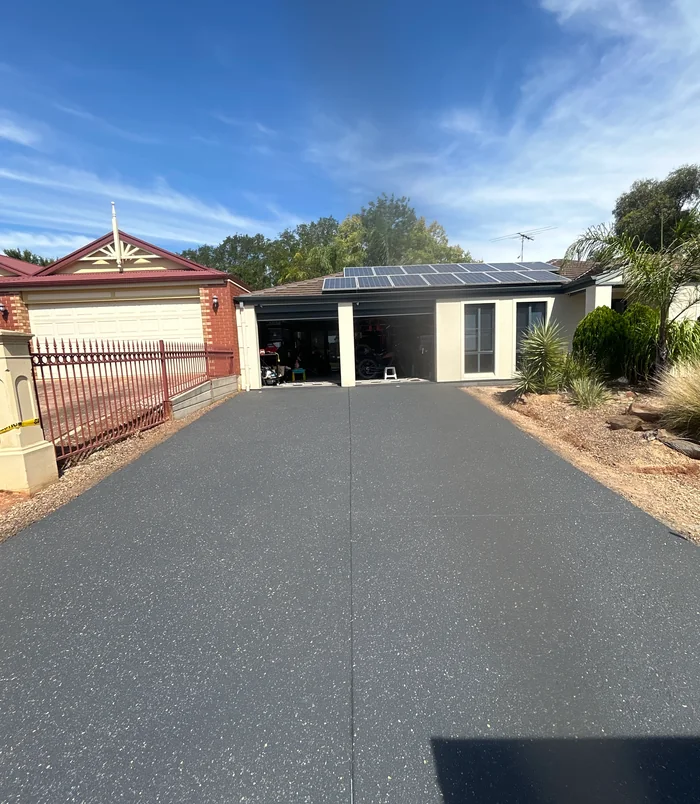 Dark grey resurfaced concrete driveway leading to a garage behind a red fence