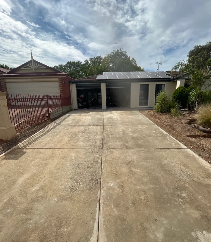 Pale, weathered concrete driveway leading to a garage behind a red fence, before concrete resurfacing