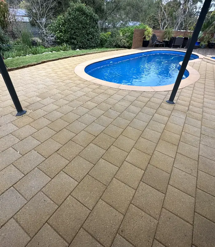 Clean, light-coloured pavers around a blue swimming pool after pressure washing
