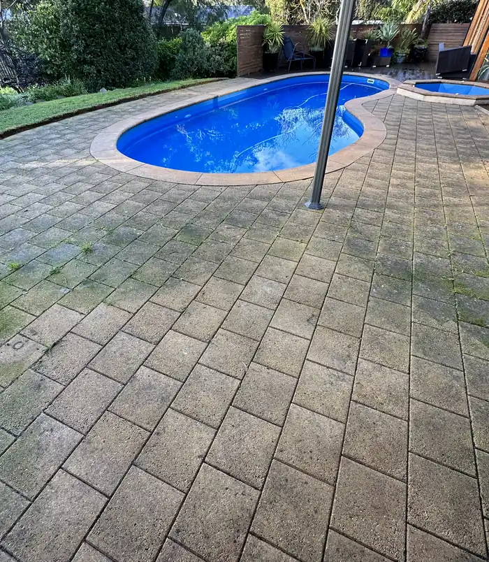 Dull, mouldy pavers around a blue swimming pool, before pressure washing