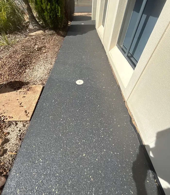 Narrow dark grey resurfaced concrete path beside a house wall and garden