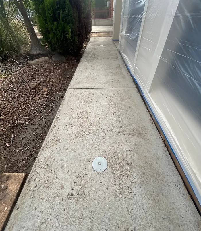 Narrow pale concrete path beside a house wall with blue masking tape, before resurfacing