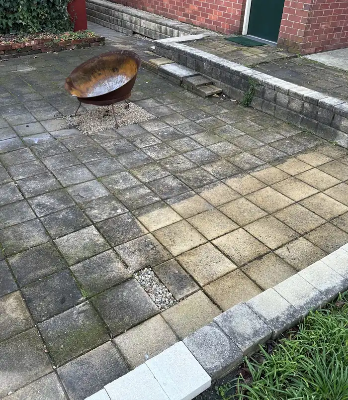 Dirty, grey-stained square pavers around a fire pit and low retaining wall, before pressure washing