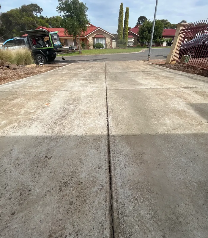 Pale, weathered concrete driveway leading to the street, before concrete resurfacing