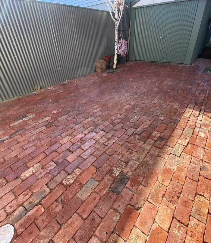 Red brick pavers in a courtyard beside a green shed, restored to rich colour after pressure washing