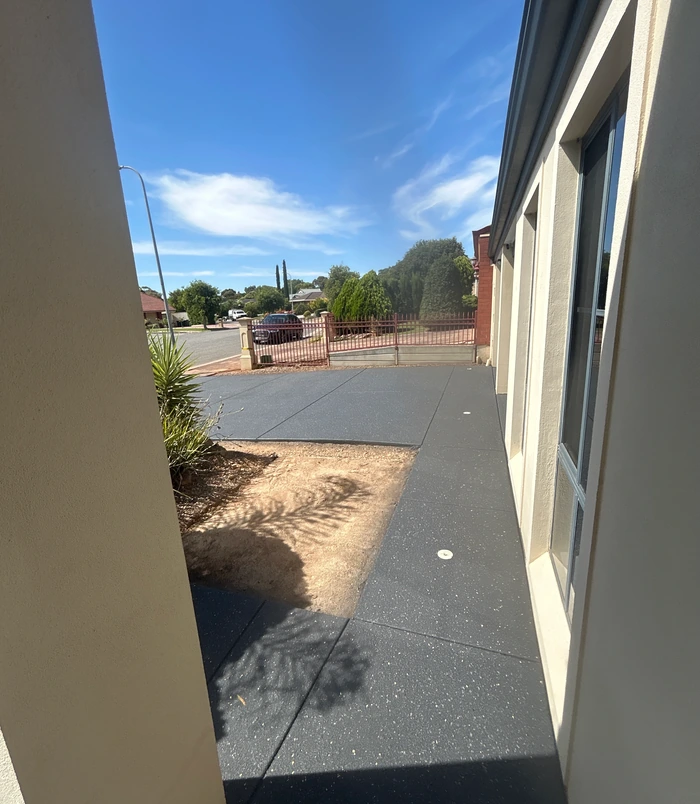 Dark grey resurfaced concrete area beside a house wall looking out to the street