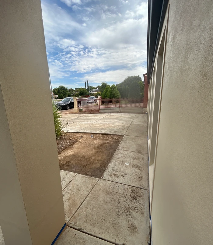 Pale, stained concrete area beside a house wall looking out to the street, before resurfacing