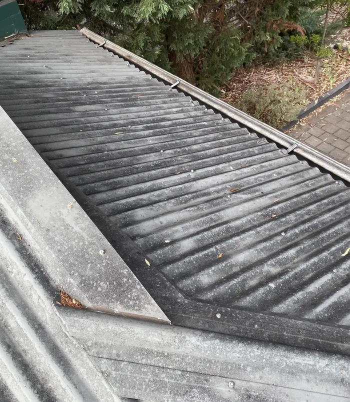Dirty, grey corrugated roof sheeting with debris along the edge, before pressure washing