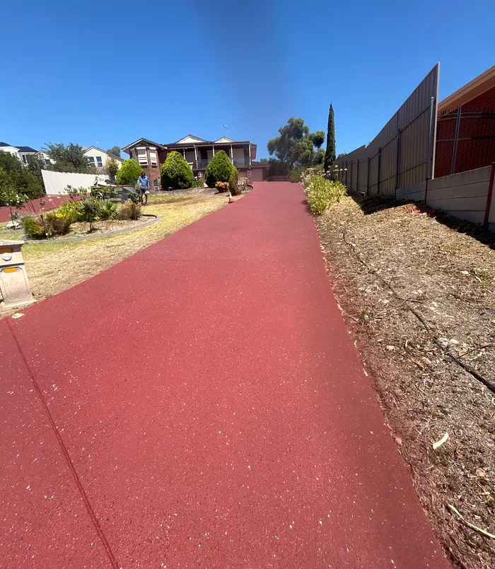 Bright red resurfaced concrete driveway beside a fence and garden bed