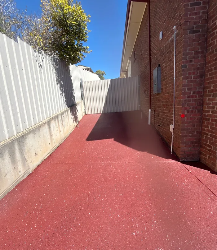 Red resurfaced concrete path beside a brick wall and white fence