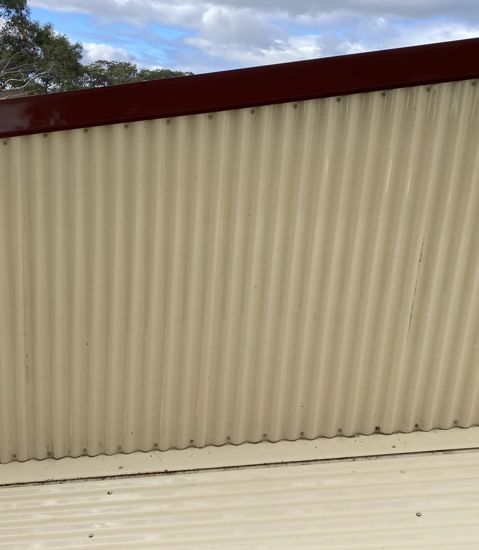 Clean corrugated metal fence with an even, light colour after pressure washing