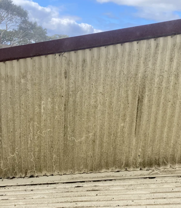 Corrugated metal fence streaked with dirt and algae, before pressure washing
