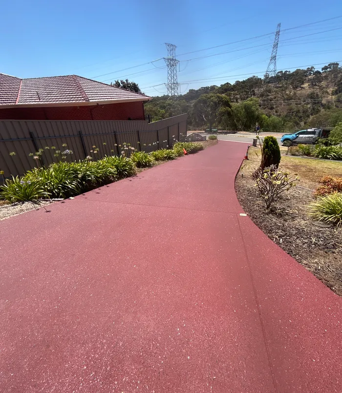 Bright red resurfaced concrete driveway curving beside a garden and fence
