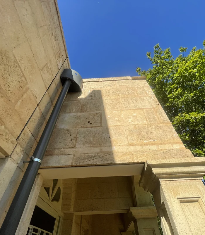 Clean, light-coloured house wall with a downpipe under a blue sky after pressure washing