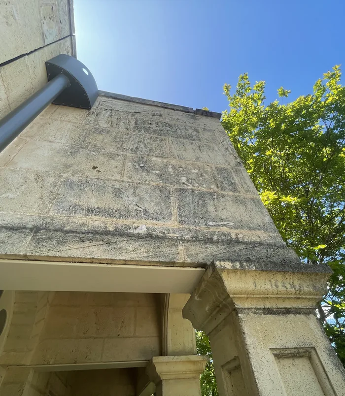 Grimy, stained house wall with a downpipe under a blue sky, before pressure washing