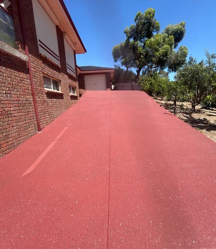 Bright red resurfaced concrete driveway beside a brick home leading to a garage