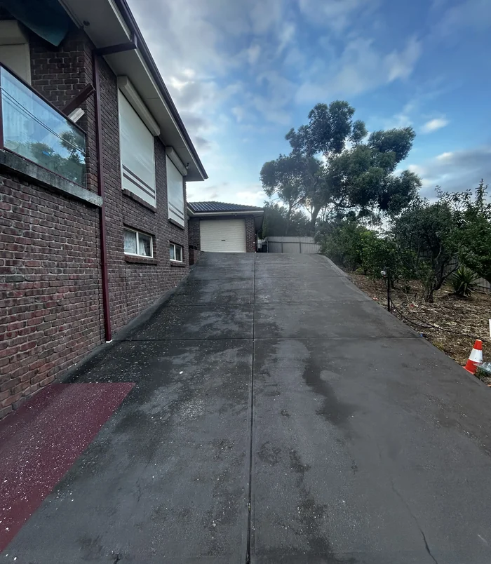 Dull, worn concrete driveway beside a brick home leading to a garage, before concrete resurfacing