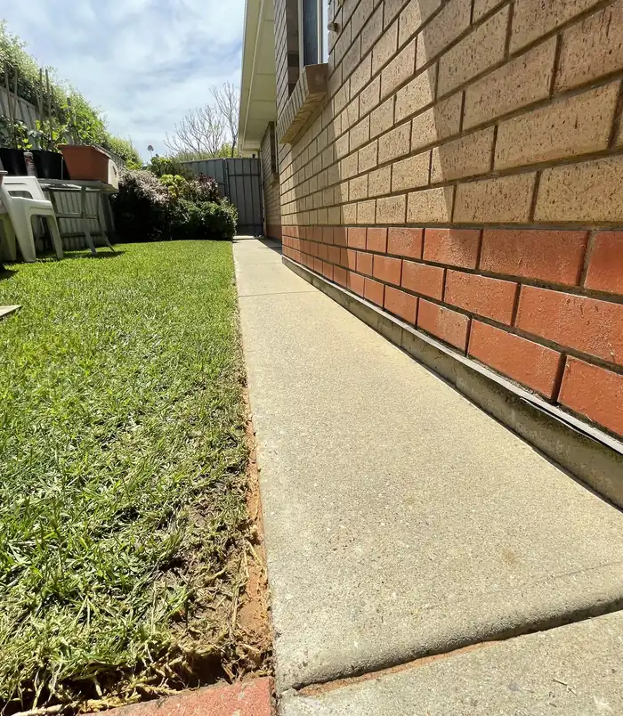 Clean, light concrete path beside a brick wall and lawn after pressure washing